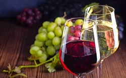 Gläser mit Rot- und Weißwein mit Trauben auf hölzernem Hintergrund