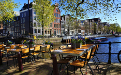Restauranttische entlang der wunderschönen Grachten von Amsterdam unter blauem Himmel im Frühling