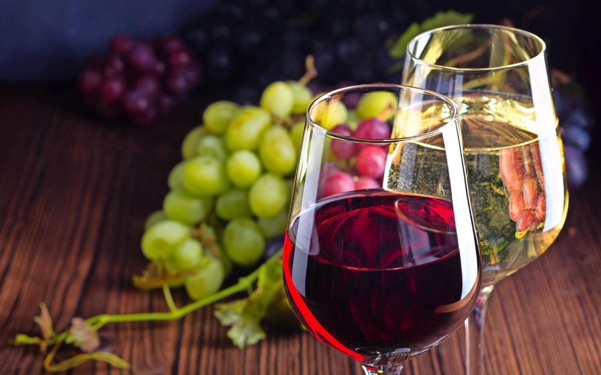 Gläser mit Rot- und Weißwein mit Trauben auf hölzernem Hintergrund