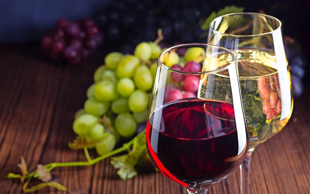 Gläser mit Rot- und Weißwein mit Trauben auf hölzernem Hintergrund