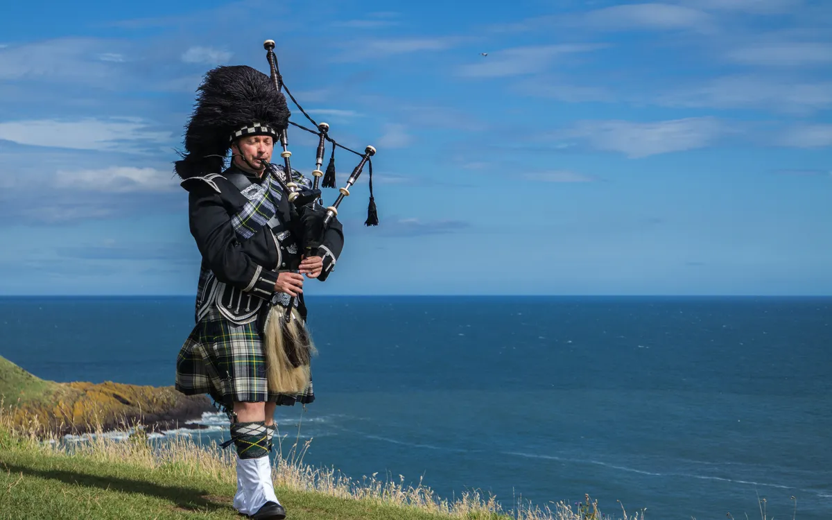 Traditionelle schottische Dudelsackspieler in voller Dresscode mit dem Meer im Hintergrund