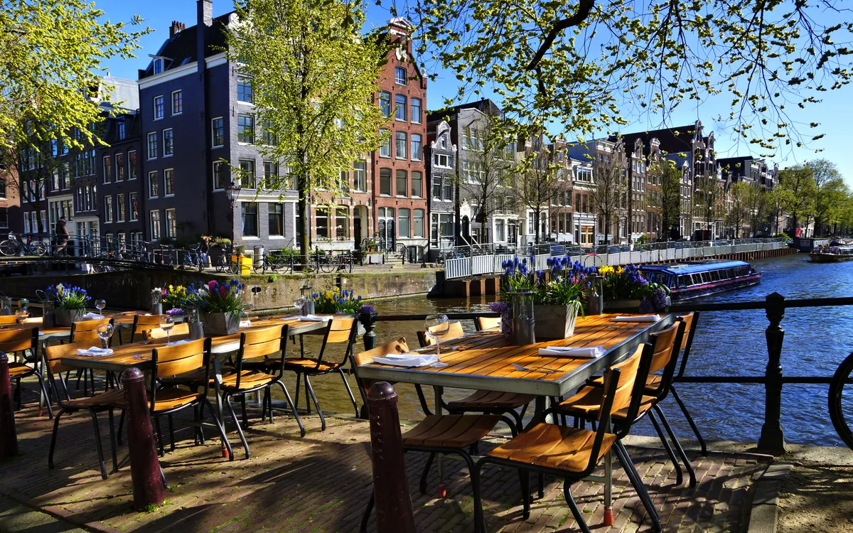 Restauranttische entlang der wunderschönen Grachten von Amsterdam unter blauem Himmel im Frühling