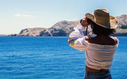 Frau schaut mit Fernglas aufs adriatische Meer
