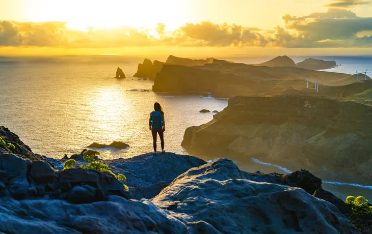 Person auf Felsklippe mit Blick auf Meer bei Sonnenuntergang.