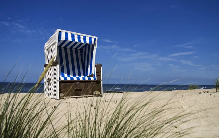 Strandkorb am Strand mit blau-weißem Himmel im Hintergrund.
