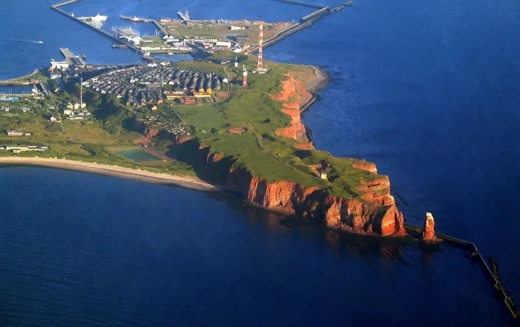 Luftaufnahme einer Insel mit Klippen, Siedlung und Hafenanlagen im Meer.