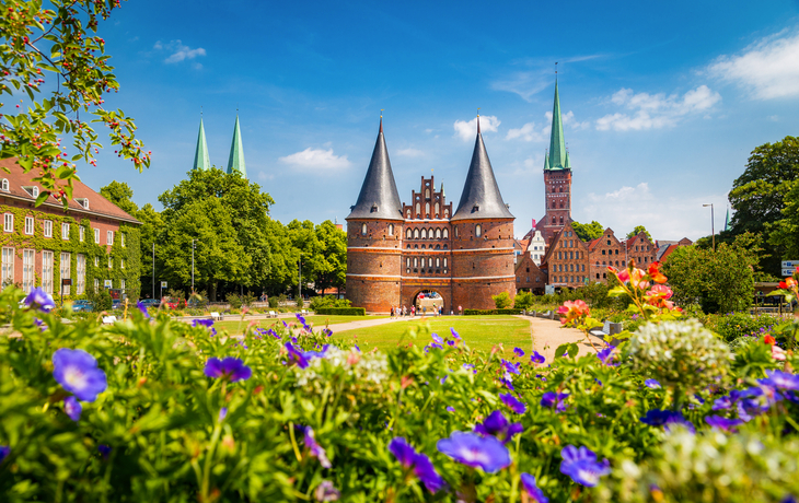 Holstentor in Lübeck mit blühenden Blumen im Vordergrund.