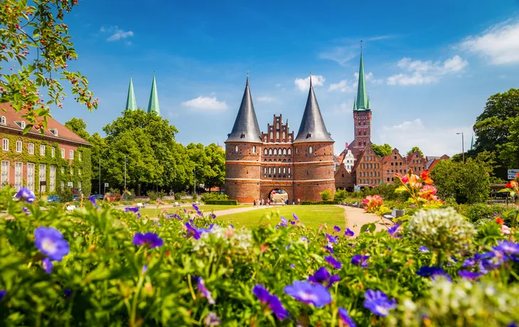 Holstentor in Lübeck mit blühenden Blumen im Vordergrund.
