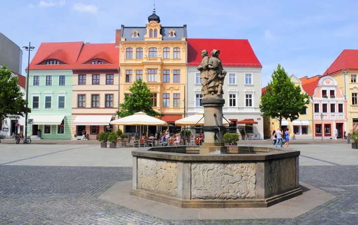 Brunnen auf einem Platz mit historischen, bunten Gebäuden im Hintergrund.