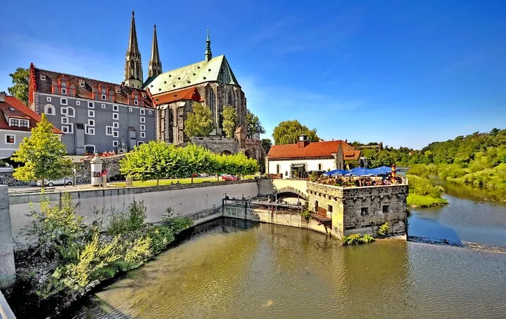Flusslandschaft mit historischer Kirche und Altstadt im Hintergrund bei sonnigem Wetter.