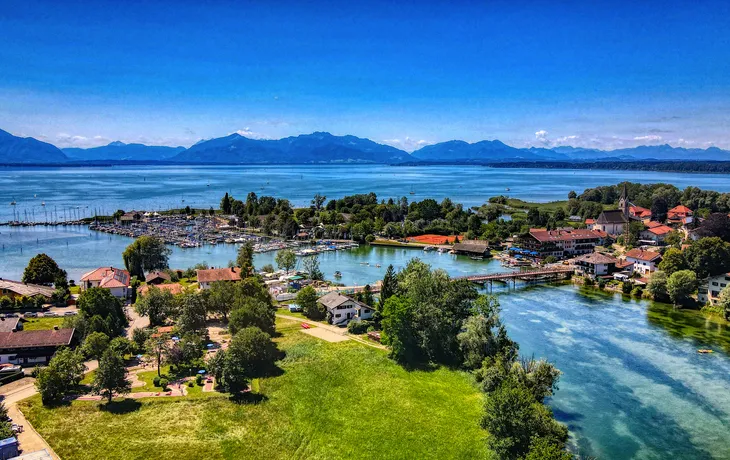 Luftaufnahme einer malerischen Landschaft mit See, Insel und Bergen im Hintergrund.