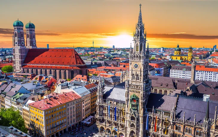 Panorama von München bei Sonnenuntergang mit historischem Rathaus im Vordergrund.