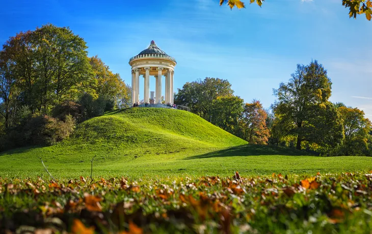 Pavillon im Englischen Garten in München, umgeben von grüner Landschaft und Bäumen im Herbst.