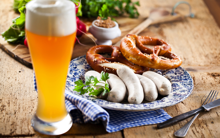 Ein Teller mit Weißwürsten, Brezen und ein Glas Bier auf einem Holztisch.