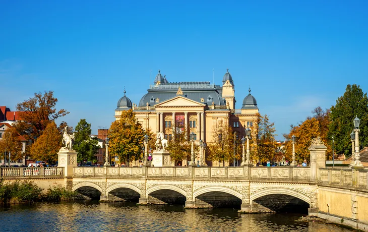 Theatergebäude hinter Fluss mit Brücke an einem sonnigen Herbsttag.