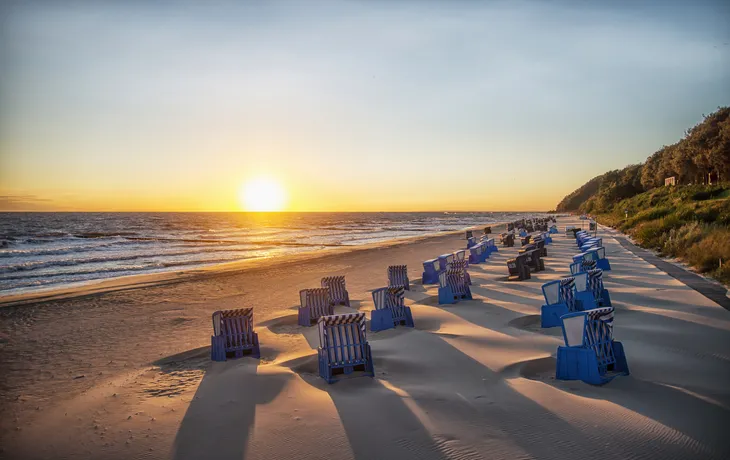Strand mit blauen Strandkörben bei Sonnenuntergang am Meer.