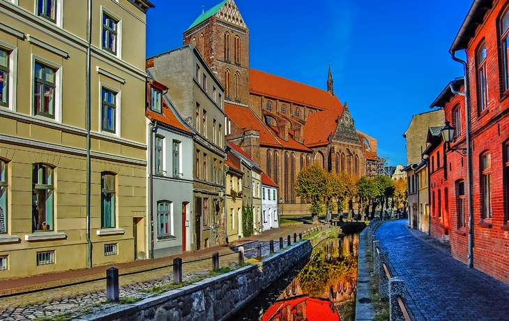 Straßenansicht mit historischem Gebäude und Wasserkanal im Vordergrund.