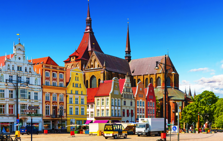 Bunte historische Gebäude und Kirche auf einem Marktplatz unter blauem Himmel.
