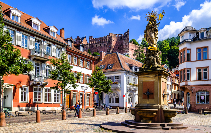 Altstadtplatz mit Springbrunnen und Schloss im Hintergrund bei sonnigem Wetter.