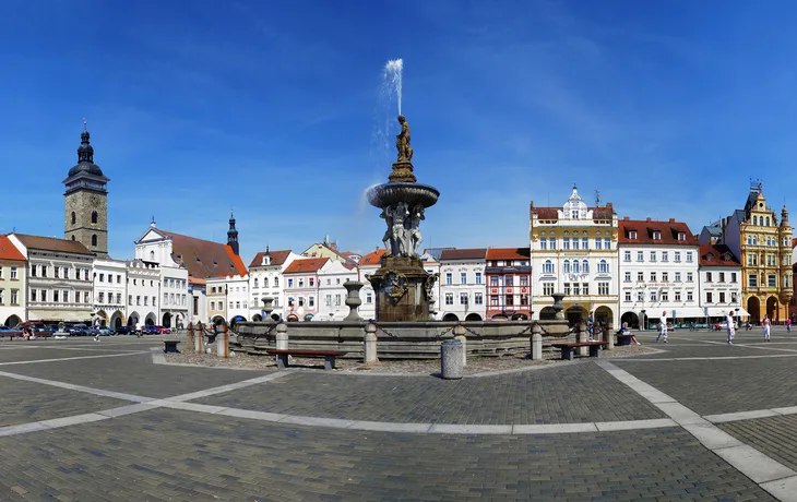 Panorama eines historischen Marktplatzes mit Brunnen und bunten Gebäuden.