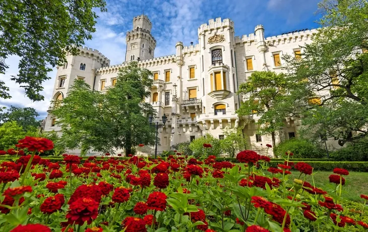 Ein Schloss mit weißen Türmen und roten Blumen im Vordergrund.