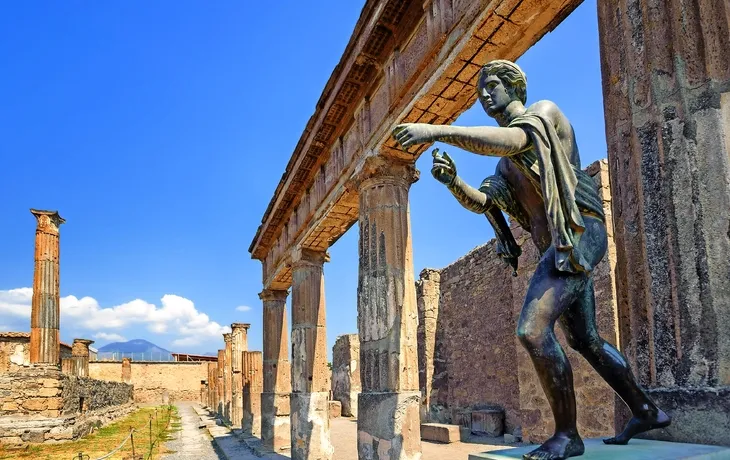 Eine antike römische Statue in den Ruinen von Pompeji vor einem blauen Himmel.

