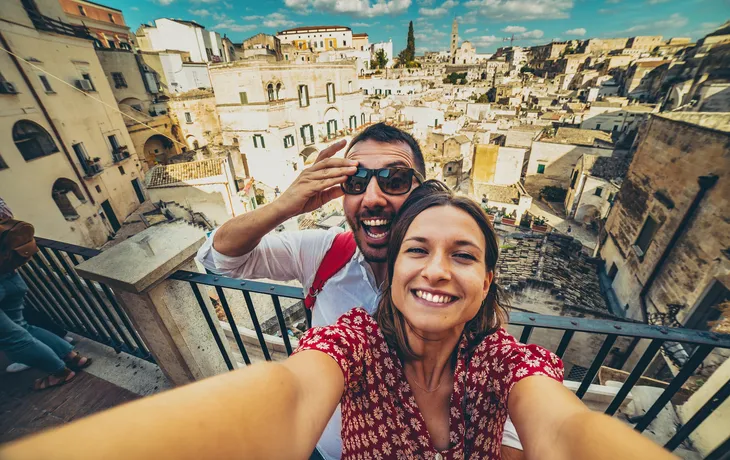 Ein Paar macht ein Selfie mit einer Altstadt im Hintergrund.