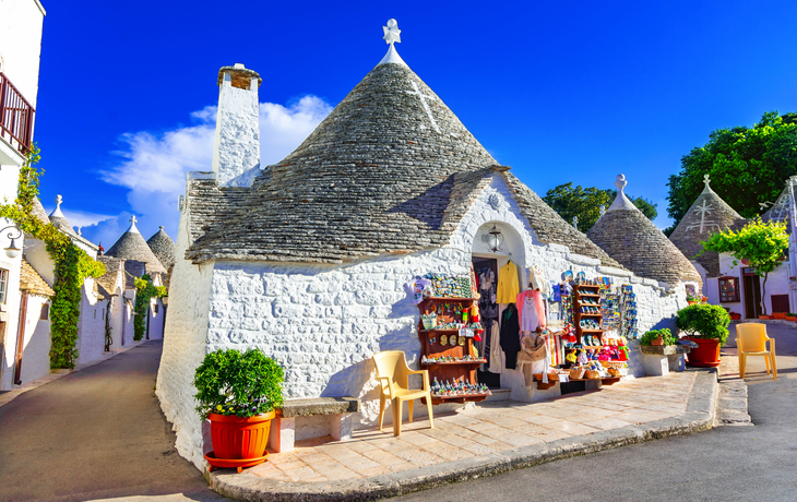 Traditionelle Trulli-Häuser mit Kegeldächern und einem Souvenirshop bei klarem Himmel.