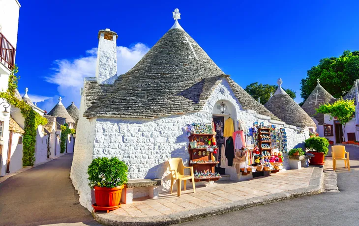 Traditionelle Trulli-Häuser mit Kegeldächern und einem Souvenirshop bei klarem Himmel.