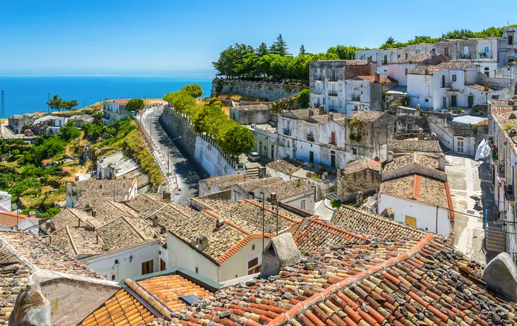 Stadtlandschaft mit traditionellen Häusern und Meer im Hintergrund bei sonnigem Wetter.