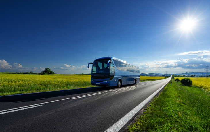 Reisebus auf Landstraße bei sonnigem Wetter.