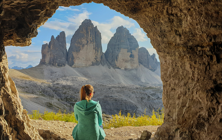 Frau in Höhle sitzend, blickt auf Drei Zinnen in den Dolomiten