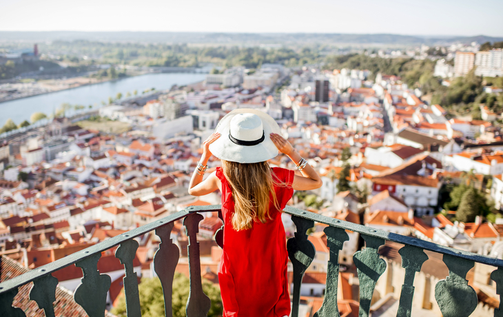 Frau in rotem Kleid und Hut blickt auf Stadtlandschaft von erhöhtem Aussichtspunkt.